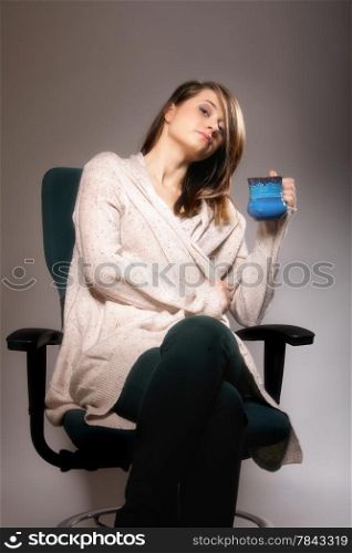 Closeup of a beautiful thoughtful sad woman holding a nice blue cup of warm beverage gray background