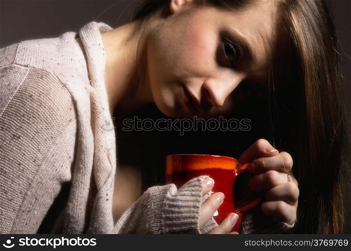 Closeup of a beautiful thoughtful sad woman holding a nice red cup of warm beverage gray background
