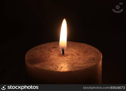 Closeup of a big burning candle , dark color