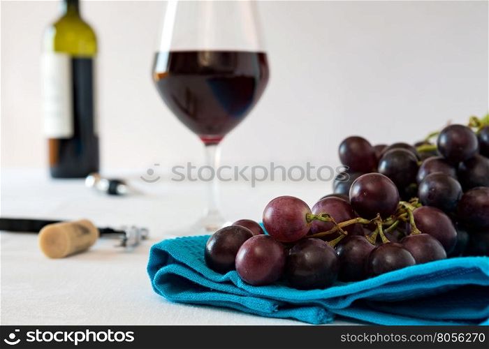 Closeup of a bunch of red grapes and a glass of red wine with a wine bottle on a blue tablecloth. Closeup of a bunch of red grapes and a glass of red wine with a wine bottle