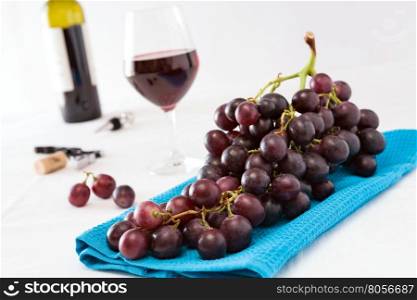Closeup of a bunch of red grapes and a glass of red wine with a wine bottle on background over a blue tablecloth. Closeup of a bunch of red grapes and a glass of red wine with a wine bottle on background
