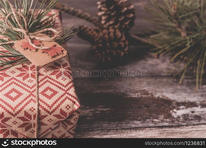 Closeup of a Christmas present with creative handmade decorative rustic diy gift wrapped in red retro wrapping paper with natural vintage twine as decor on old wood floor with spruce twig and pinecones in the background with copyspace.