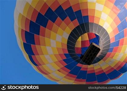 Closeup of a colorful hot-air balloon in flight seen from below against a blue sky. Closeup of a colorful hot-air balloon in flight seen from below