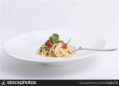 Closeup of a delicious looking spaghetti dish with basil, tomato sauce and shredded herbs on a light background. Vegetarian and culinary concept.. Spaghetti dish with basil, tomato and shredded herbs