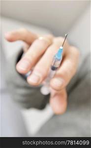 Closeup of a hand holding an injection for vaccination. Focus on tip of needle
