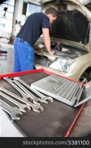 Closeup of a laptop and wrench and man mechanic working in background
