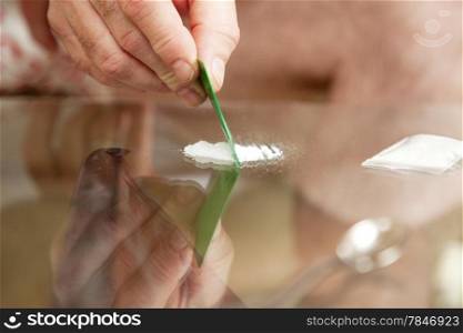 Closeup of a man&rsquo;s hand cutting cocaine on a glass table with a credit card.