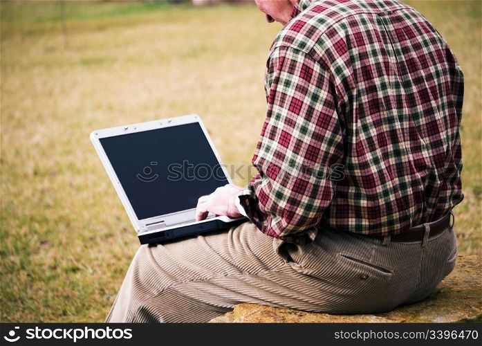 Closeup of a man working on a computer outside.
