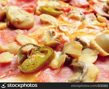 Closeup of a pizza with chili peppers, ham and mushrooms.