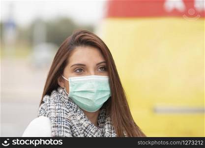 Closeup of a sad looking woman using a green surgical mask on an out of focus background. Sickness and prevention concept.. Closeup of a sad looking woman wearing a mask