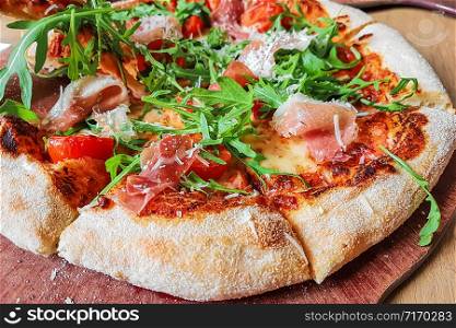 Closeup of a traditional italian pizza with: ham, mushrooms, cherry tomatoes, mozzarella, arugula on a wooden board ( high details).