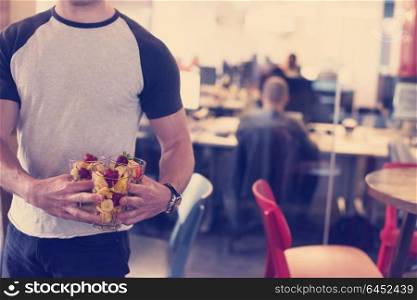closeup of a young software developer eating a fruit salad from a clear cup at the startup office