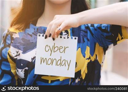 Closeup of a young woman outdoors showing a notepad with the text "cyber monday" written in it. Discount and sale concept