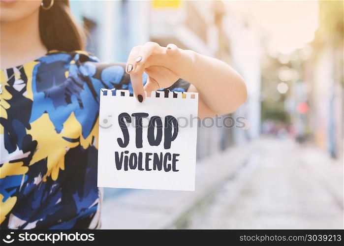 "Closeup of a young woman outdoors showing a notepad with the text "stop violence" written in it.. Young woman showing a notepad with the text "stop violence" "