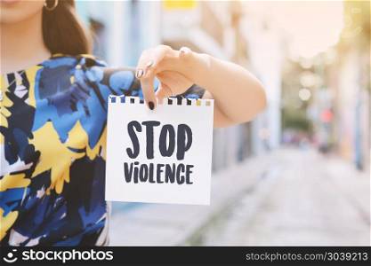 "Closeup of a young woman outdoors showing a notepad with the text "stop violence" written in it.. Young woman showing a notepad with the text "stop violence" "