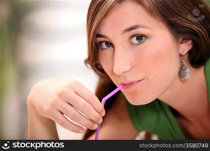 Closeup of a young woman sucking a pink straw