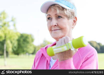 Closeup of active senior woman lifting dumbbells in park
