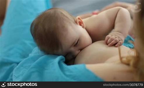 Closeup of adorable infant child breast feeding. Cute baby girl with arm on mother&acute;s chest falling asleep while breastfeeding.