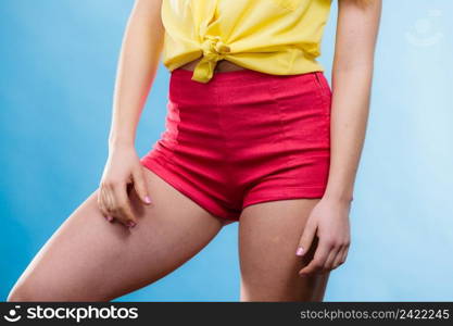 Closeup of alluring woman hips. Slim girl wearing yellow shirt and red shorts on blue. Summer fashion.. Closeup woman hips in shorts