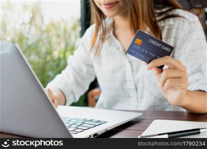 Closeup of Asian businesswoman typing on laptop keyboard while holding credit card, Women shopping online or booking a ticket on notebook. Business, technology and lifestyle concept.