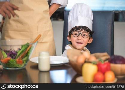 Closeup of Asian cute little boy wearing chef hat and apron with mother in home kitchen. Thai people and lifestyles concept. Job occupation and Education learning concept. Happy family time theme