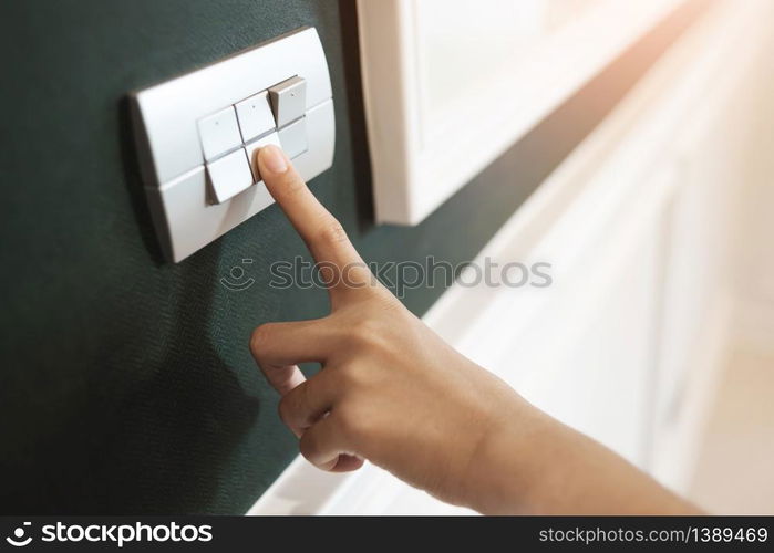 Closeup of Asian female right hand is turning on or off on grey light switch over green wall. Copy space.