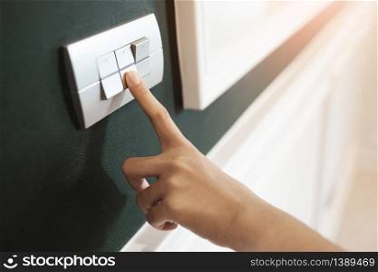 Closeup of Asian female right hand is turning on or off on grey light switch over green wall. Copy space.