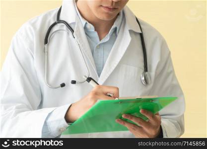 Closeup of asian male doctor writing health report,Medical care or prescription on the green clipboard in hospital. Concept of Medical and healthcare.