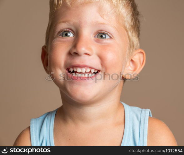 Closeup of Baby boy smiling three year old, blond with green eyes on a light brown background, conceptual photo for dental hygiene and personal care.