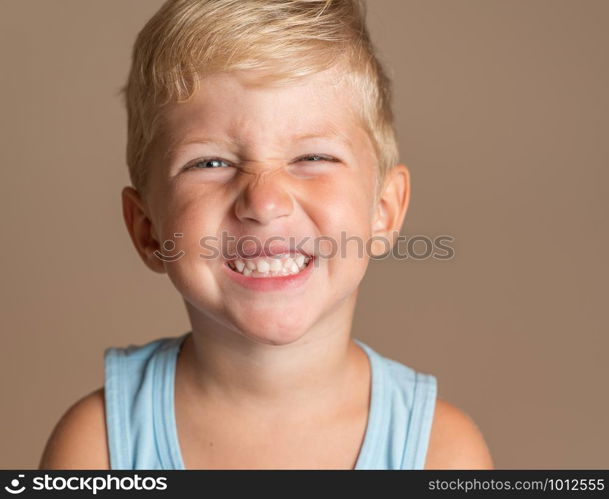 Closeup of Baby boy smiling three year old, blond with green eyes on a light brown background, conceptual photo for dental hygiene and personal care.