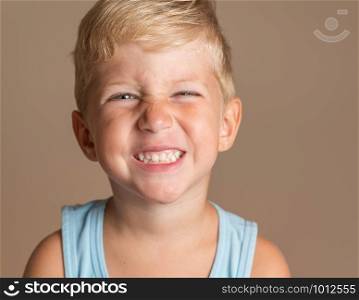 Closeup of Baby boy smiling three year old, blond with green eyes on a light brown background, conceptual photo for dental hygiene and personal care.