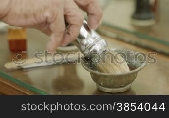 Closeup of barber&acute;s hand preparing shaving cream with brush in barber shop or male beauty parlor