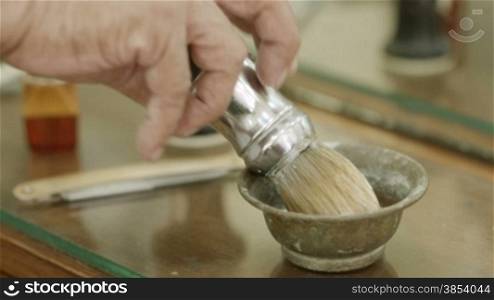 Closeup of barber&acute;s hand preparing shaving cream with brush in barber shop or male beauty parlor