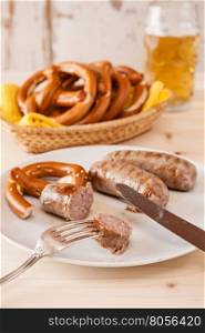 Closeup of bavarian cooked sausage and pretzel on a breadbasket and beer on background. Closeup of bavarian cooked sausage and pretzel