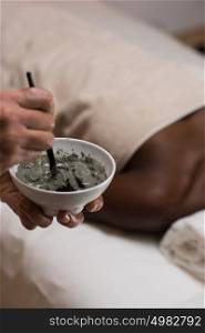Closeup of beautician hands are mixing and applying clay facial mask to african woman