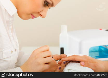 Closeup of beautician painting nails of female client. Woman in beauty spa salon doing manicure. Woman in beauty salon getting manicure done.