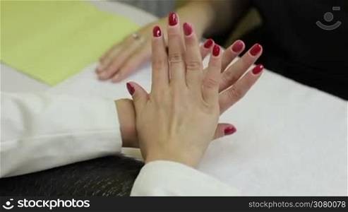Closeup of beautiful female hands with red nails. Woman showing perfect clean red gel manicure with zero cuticle in beauty salon. Back view. Gorgeous young woman getting her nails done by manicurist.