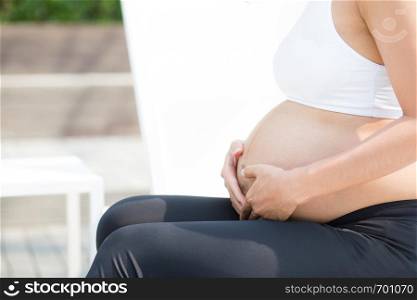 Closeup of beautiful pregnant asian young woman relax in the park, girl with belly sitting at swimming pool for wellness, tummy girl, health care concept.