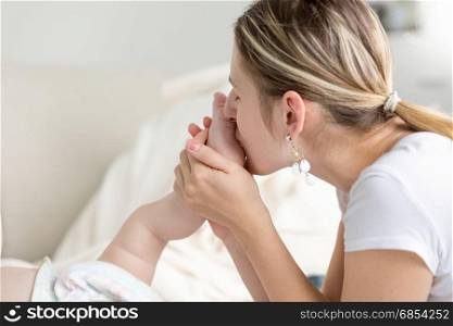 Closeup of beautiful young mother kissing baby foot