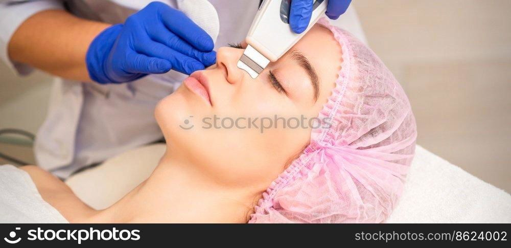 Closeup of beautiful young woman receiving ultrasound facial exfoliation and cavitation facial peeling with ultrasonic equipment in cosmetology office. Closeup of beautiful young woman receiving ultrasound facial exfoliation and cavitation facial peeling with ultrasonic equipment in cosmetology office.