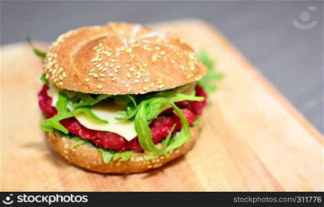 Closeup of beetrot burger with grilled arugula on wooden plate.
