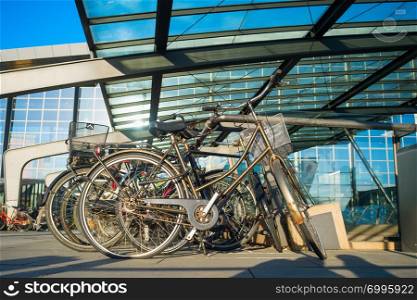 Closeup of bicycles on parking by Kastrup International airport under glass canopy in sunshine day, Copenhagen, Denmark
