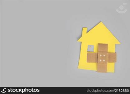 Closeup of broken house figure with crossed band aid on grey background top view, copy space, divorce, relationship problems, moving house, mortgage, space for text. Closeup of broken house figure with crossed band aid on grey background top view, copy space, divorce, relationship problems, moving house, mortgage,