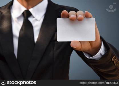 Closeup of businessman showing white piece of paper in black suit. Idea for business credit card or visiting card.