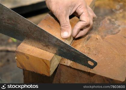 Closeup of carpenter cutting plank with hand saw