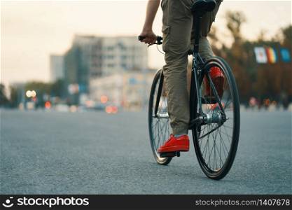 Closeup of casual man legs riding classic bike on city gray road wearing red sneakers and comfy pants. Copy space. Closeup of casual man legs riding classic bike on city road