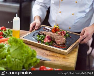 closeup of Chef hands in hotel or restaurant kitchen serving beef steak with vegetable decoration. closeup of Chef hands serving beef steak