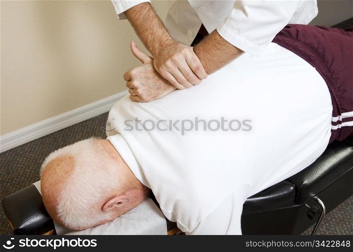 Closeup of chiropractors hands doing spinal adjustment on senior man.