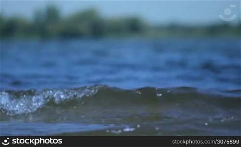 Closeup of clear water surface with ripples low waves on blurred landscape background . Horizontal shot