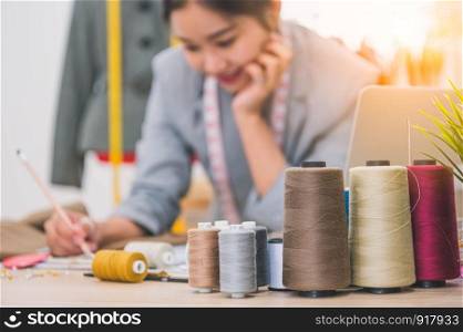 Closeup of color thread with blurry happy female tailor and sewing clothing stylist designer background. Woman creating new collection in workshop office. People lifestyle and freelance occupation job